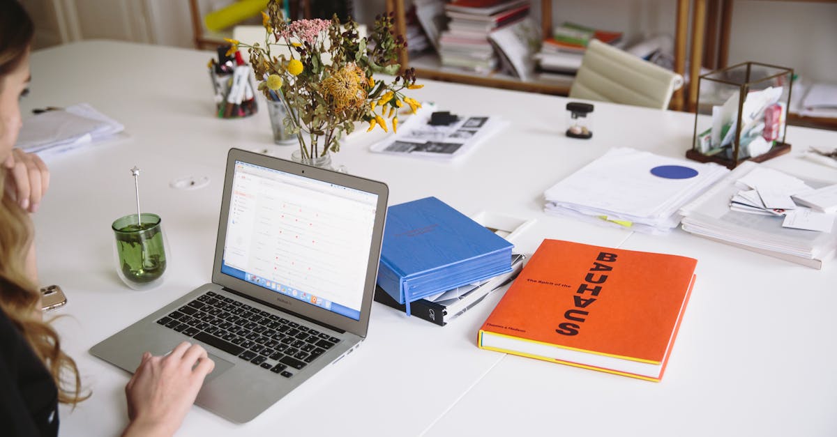 Woman works on a laptop in a stylish office, surrounded by books and documents.